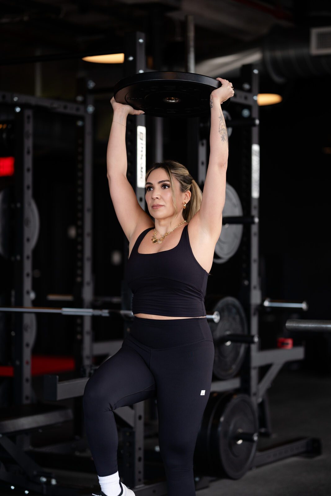 Carolina pressing a weight plate overhead in the gym